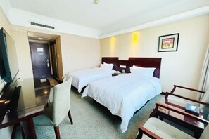 Ein Hotelzimmer mit zwei Betten, einem Schreibtisch, einem Sessel und einem kleinen Tisch.