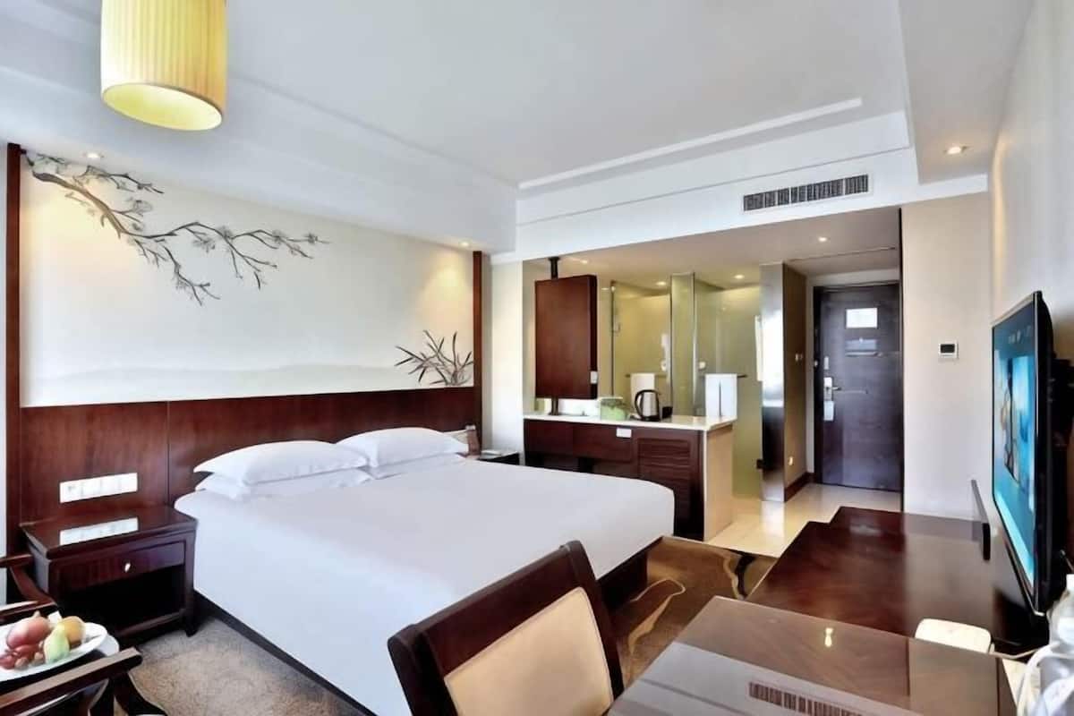 A hotel room with a large bed, a desk with a chair, a television, a mirror, and a wall-mounted artwork.