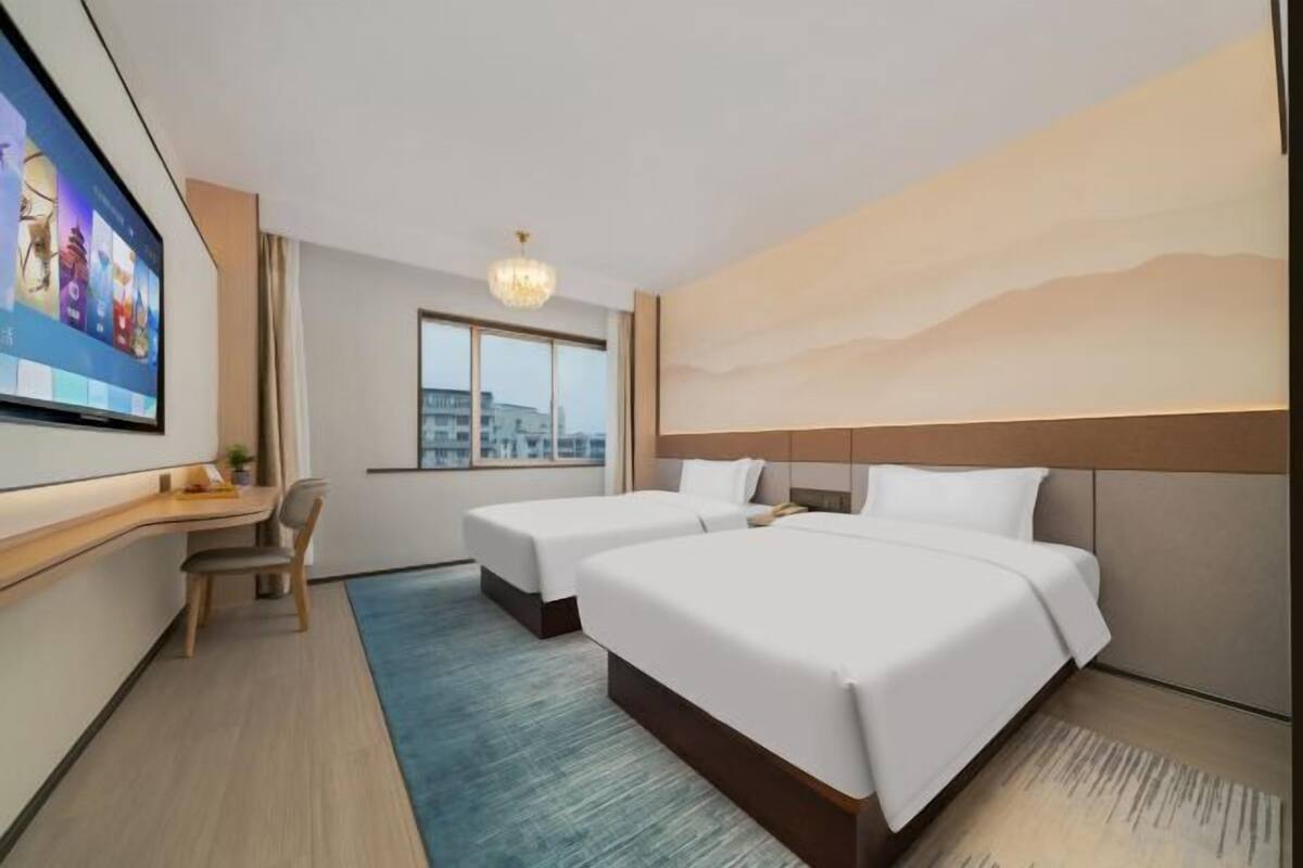 Ein Hotelzimmer mit zwei Betten, einem Schreibtisch, einem Sessel, einem Fernseher und einem großen Fenster.