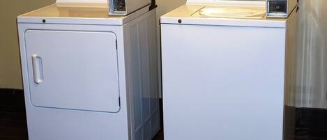 Two white front-loading washers with control panels, placed side by side in a room with tiled flooring.