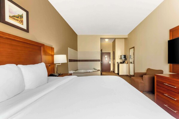 Une chambre d’hôtel avec un grand lit, un coin salon comprenant un fauteuil et une table, une télévision et une salle de bain avec baignoire.