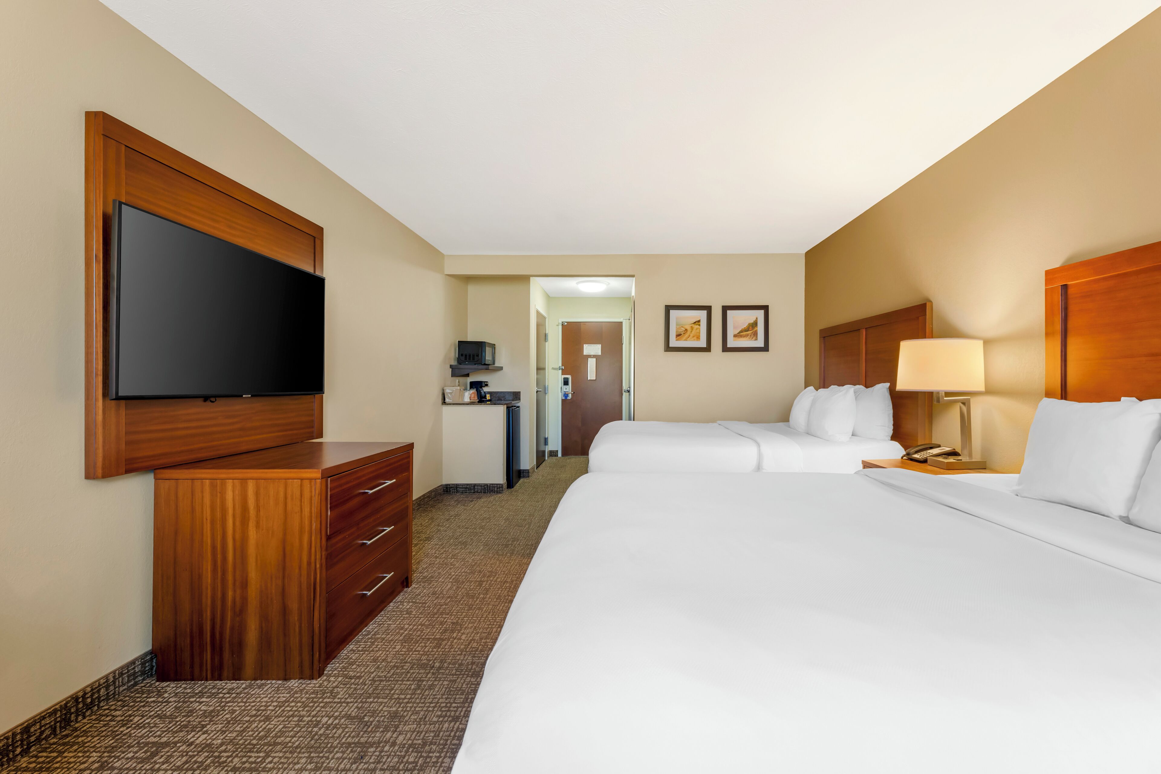 Een hotelkamer met een groot bed, een aan de muur bevestigde televisie, een bureau met een lamp en een deur naar een gang.