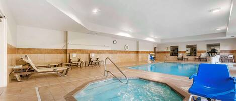 An indoor swimming pool with lounge chairs and a jacuzzi area.
