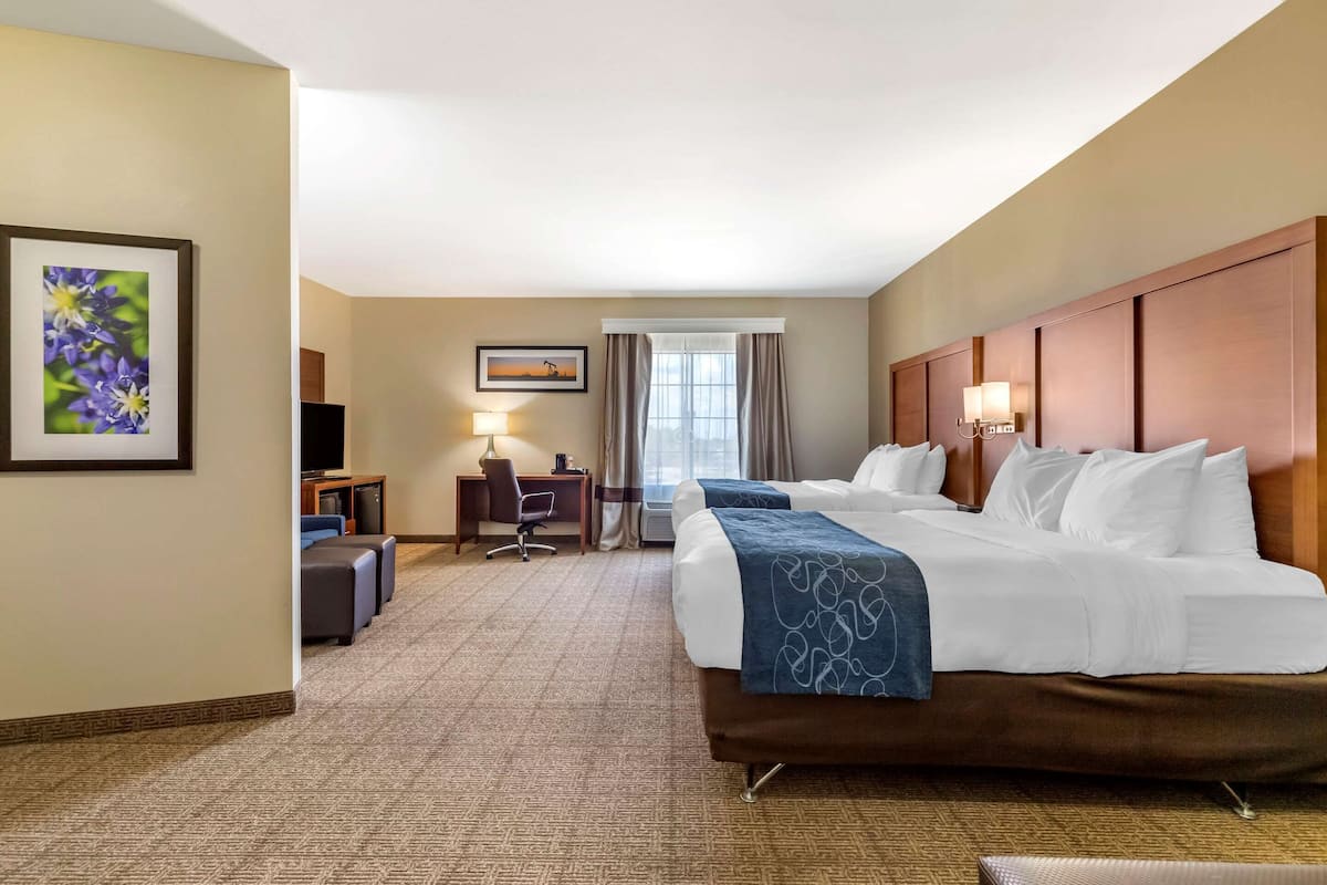 Quarto de hotel com uma cama grande, uma escrivaninha com cadeira, uma televisão e uma janela com cortinas.