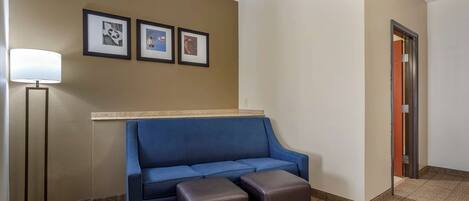 A room with a blue sofa, two brown ottomans, a standing floor lamp, and three framed pictures on the wall.