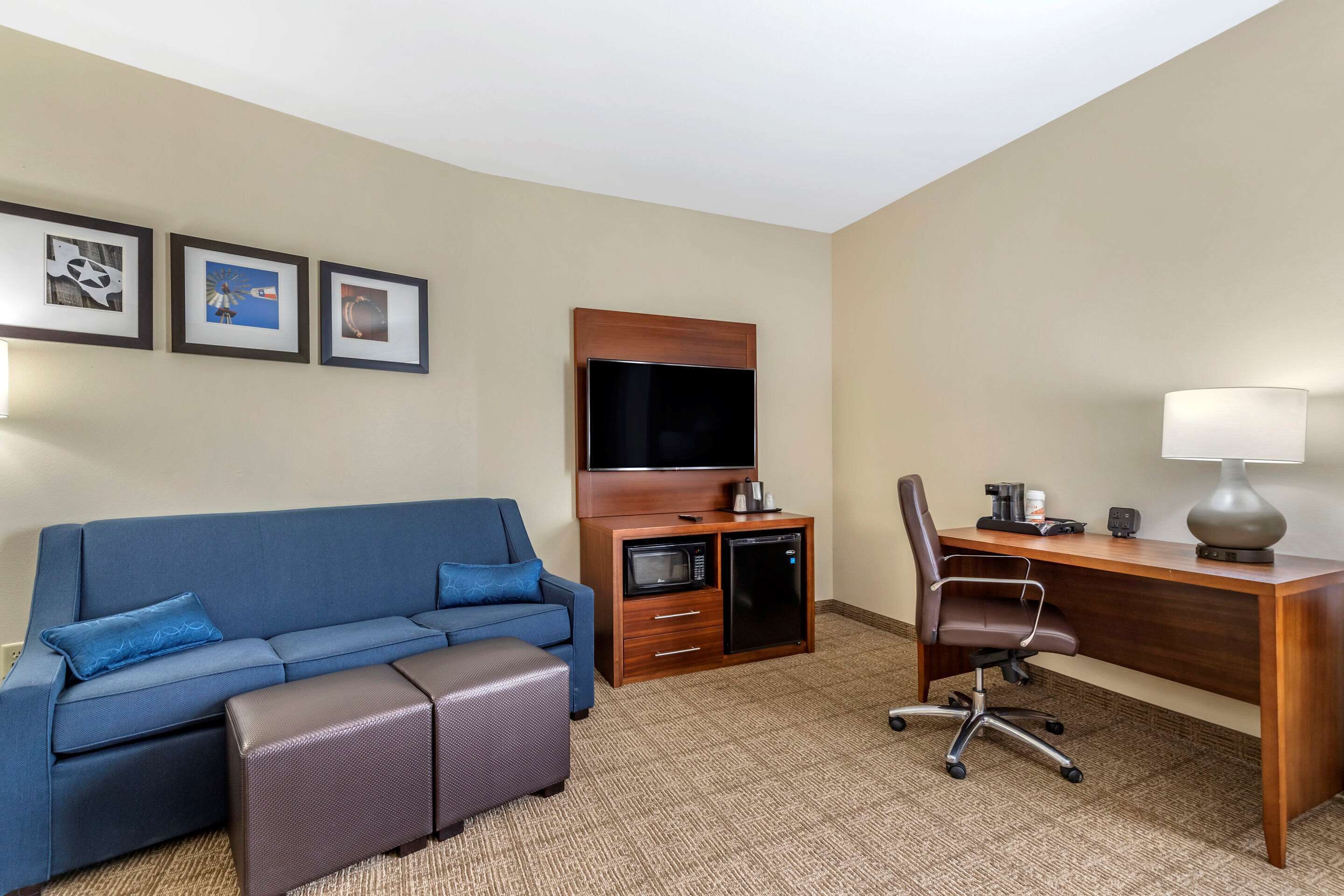 Ein Hotelzimmer mit blauem Sofa, Schreibtisch aus Holz, Fernseher, Mikrowelle und Kaffeemaschine.