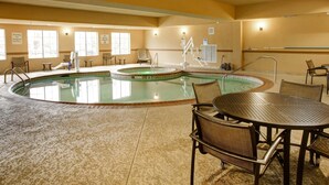 A hotel pool area with multiple pools, sun loungers, and a table with chairs.
