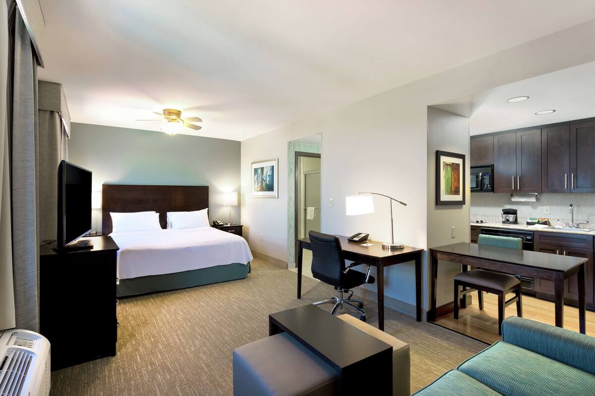 A hotel room with a bed, desk, chair, and kitchenette.