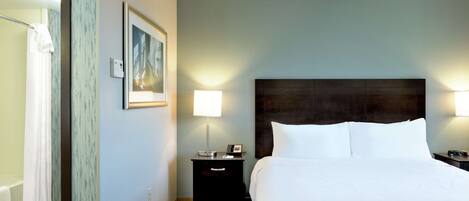 A hotel room with a bed, nightstands, a lamp, a painting, and a ceiling fan.
