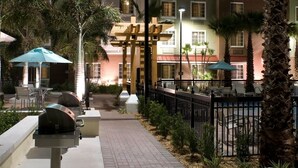 Un patio de hotel con mobiliario exterior, palmeras y una estructura de madera en el centro.