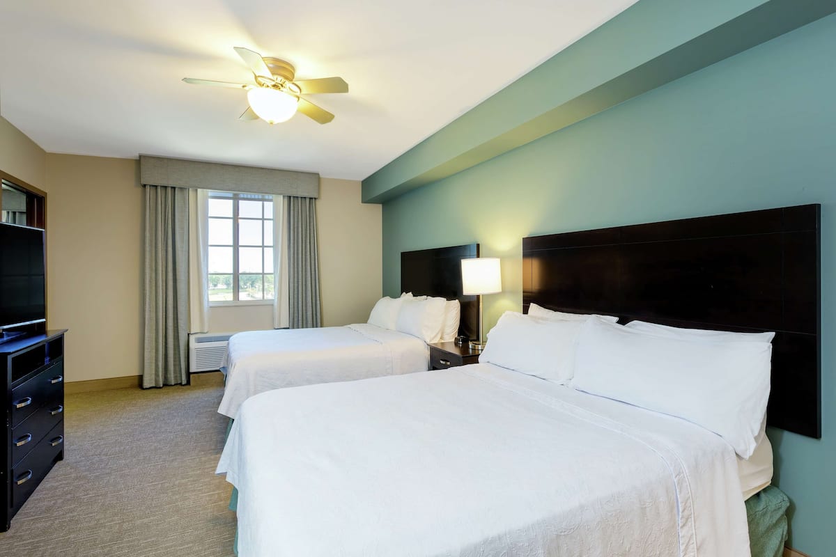 A hotel room with two beds, a ceiling fan, a TV, and a window with curtains.