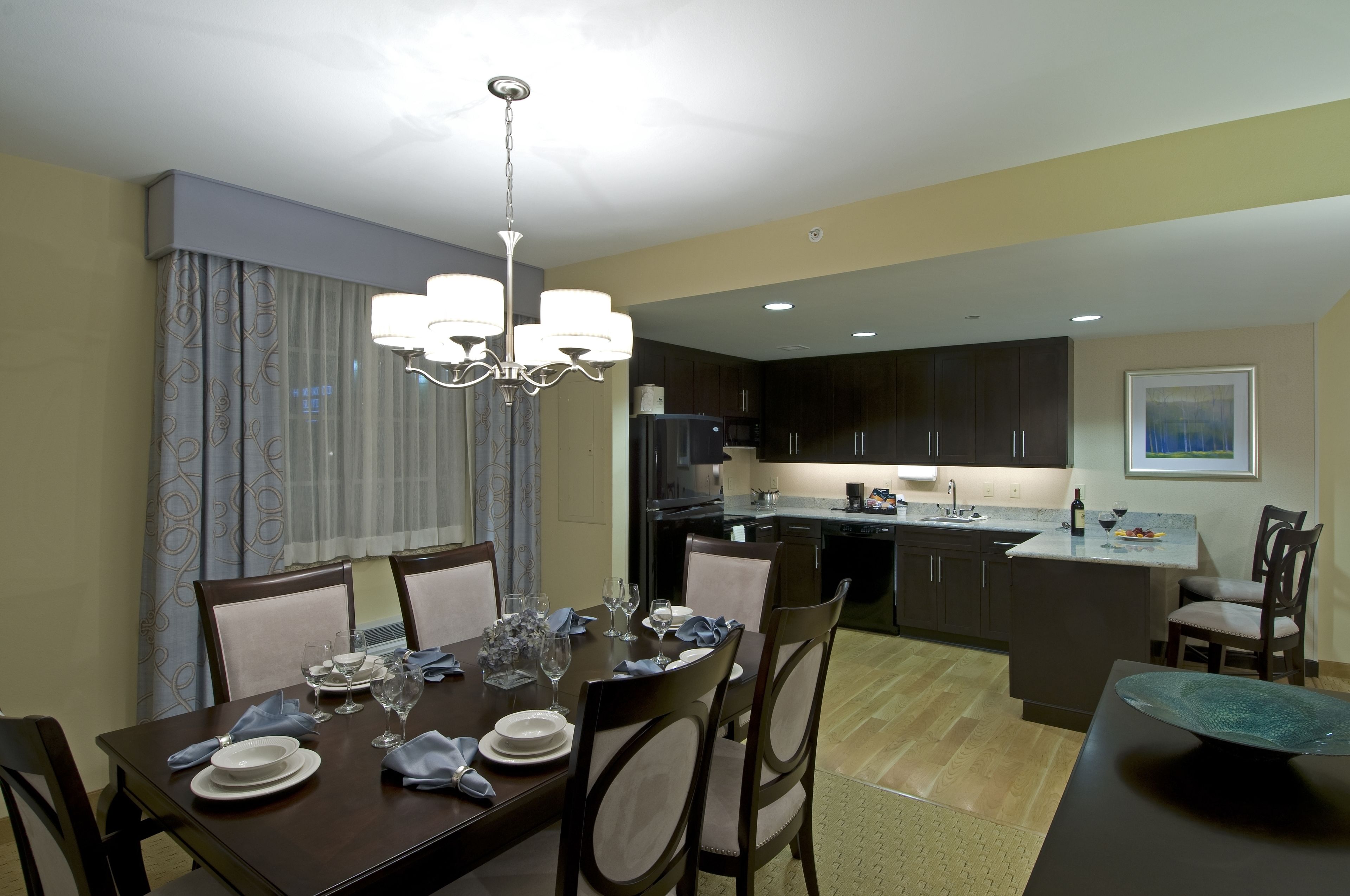 A dining area with a table set for four, a chandelier, and a kitchen in the background.