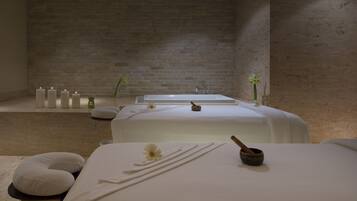 Un cuarto de spa con dos camillas de masaje, velas y una pared de piedra.