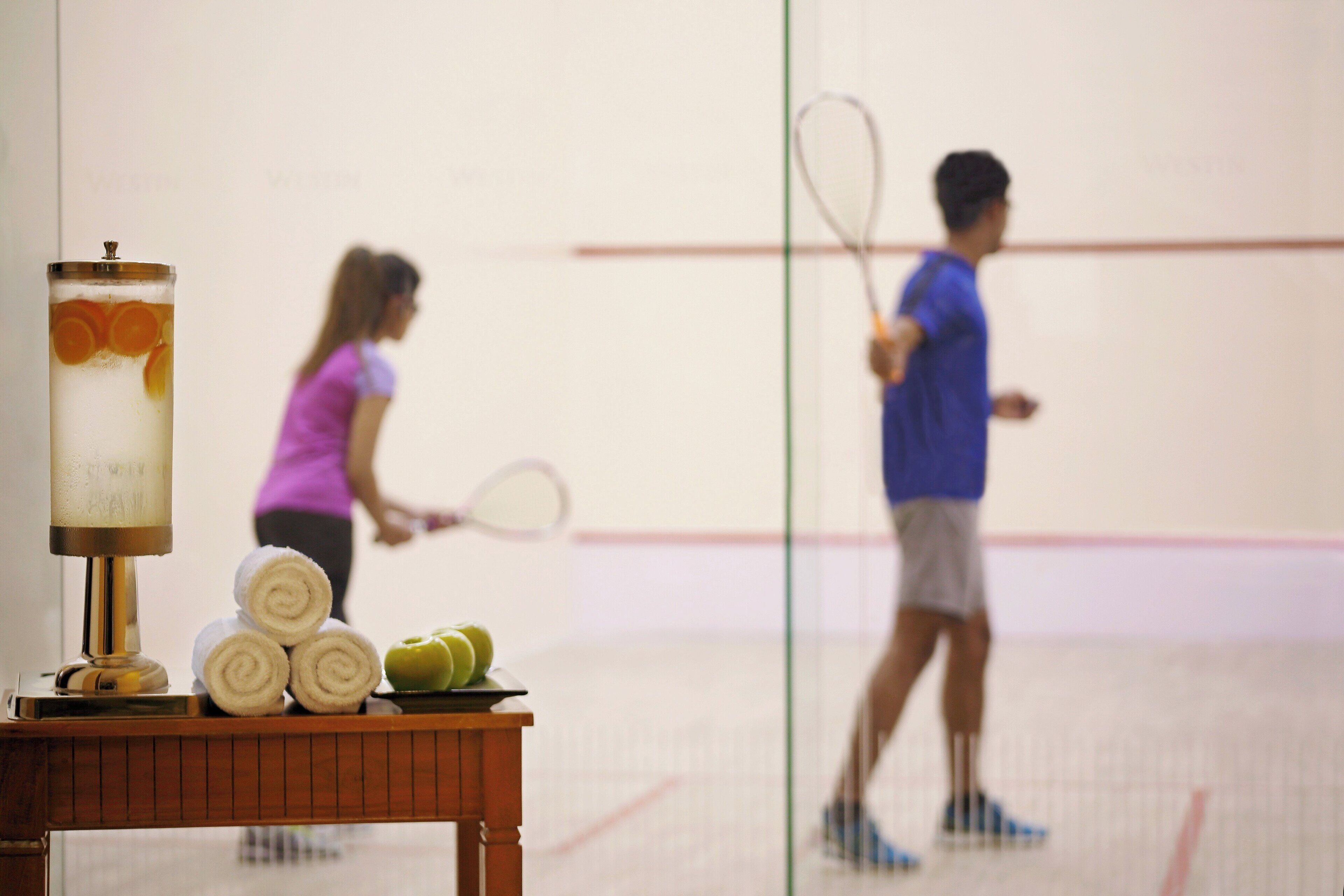 Una cancha de squash con una mesa al frente que sostiene toallas y una botella de agua.