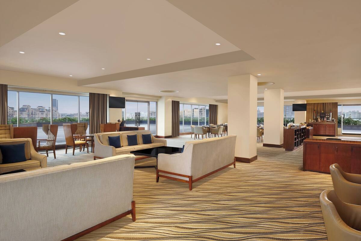 Un amplio hall de hotel con una gran zona de estar, un bar y vistas a la ciudad a través de amplias ventanas.