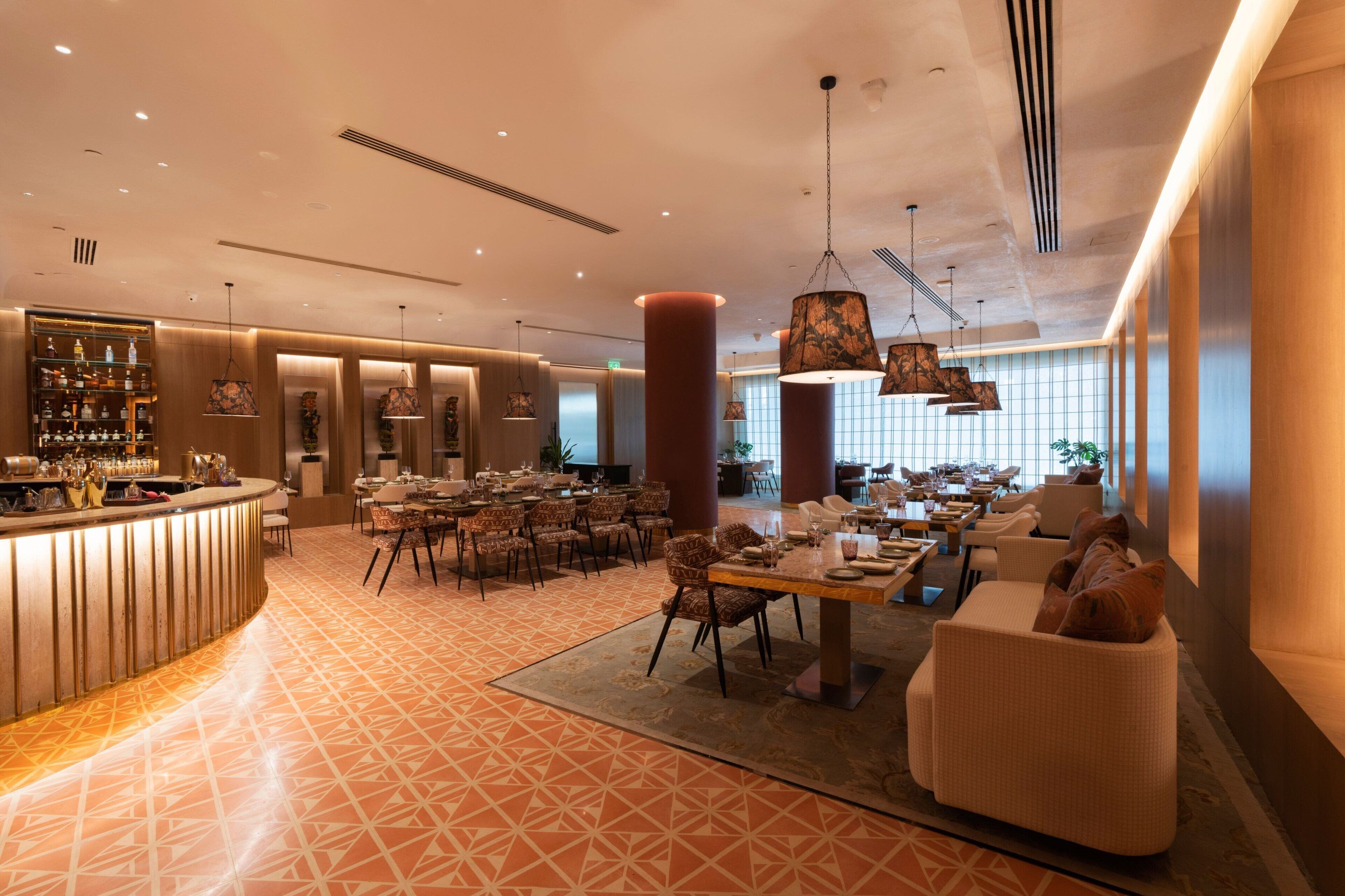 A spacious hotel lobby with a bar area, multiple dining tables, and comfortable seating.