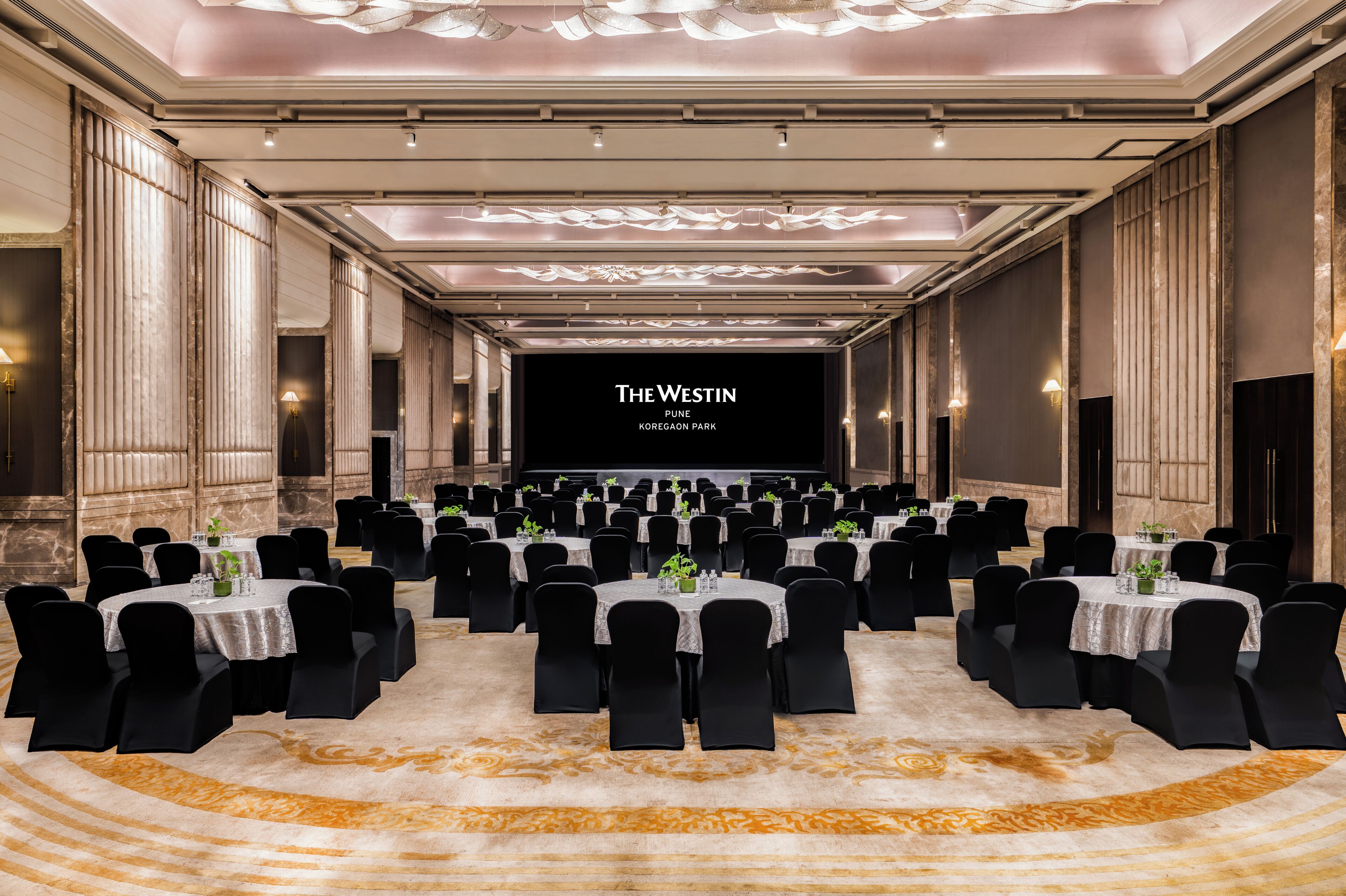 Ett konferensrum på The Westin Pune med en scen, flera runda bord och svarta stolar.