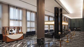 A spacious lobby with a marble floor, a reception desk, and a seating area with tables and chairs.