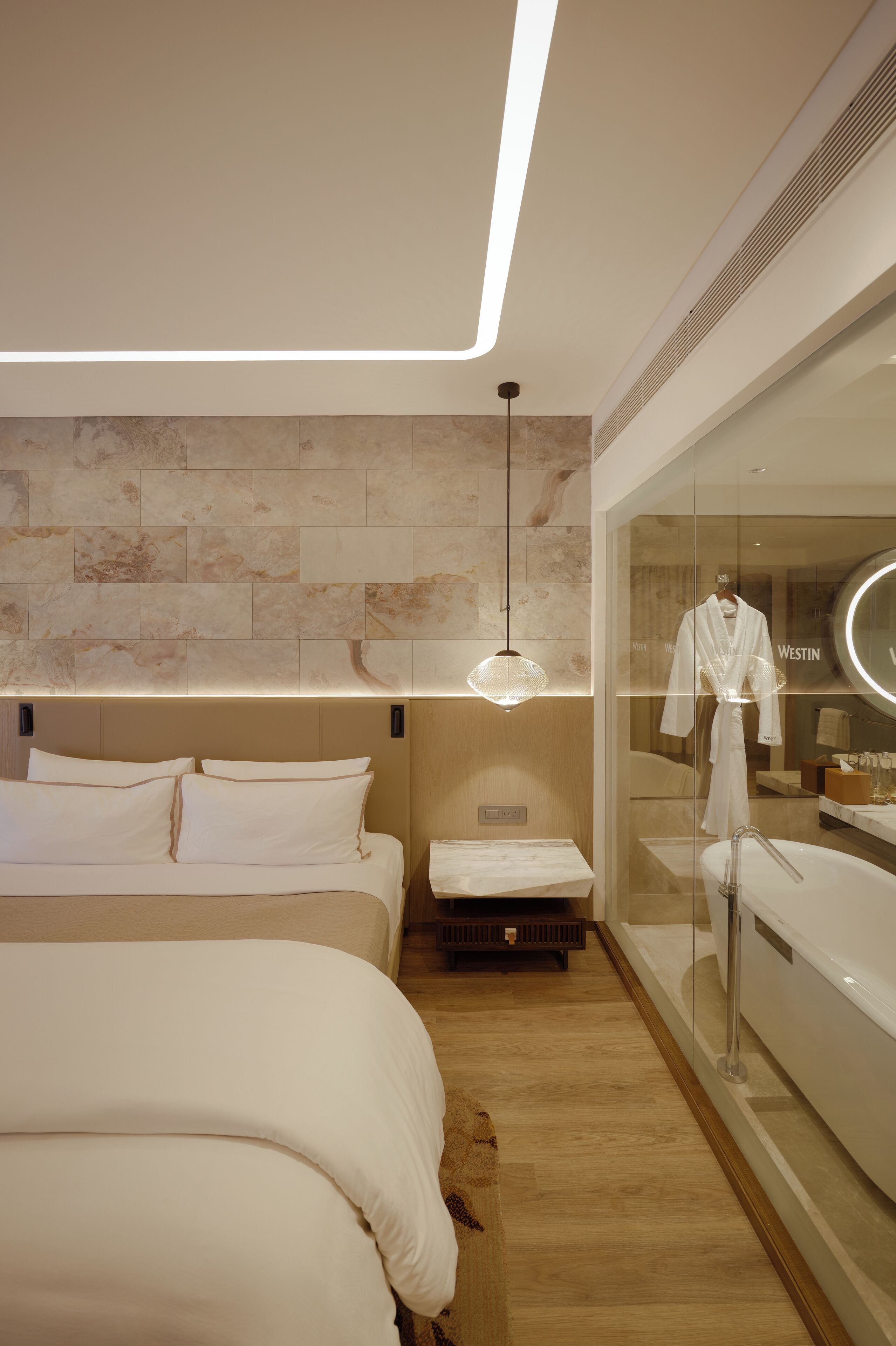 A modern hotel room with a large bed, a glass partition with a robe, and a wooden floor.