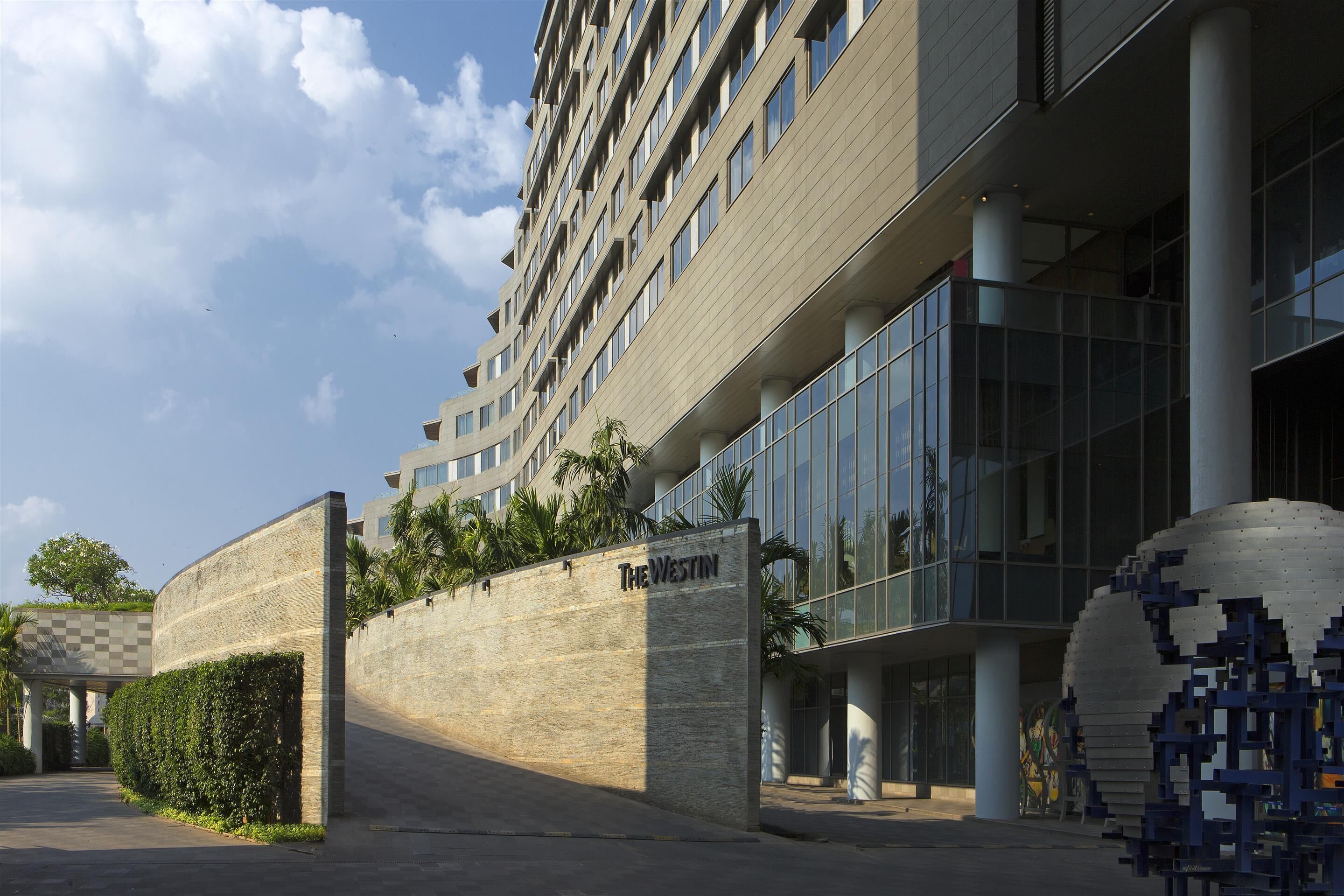 A modern hotel entrance with a stone wall, a sign reading "The Westin", and a glass building with columns.