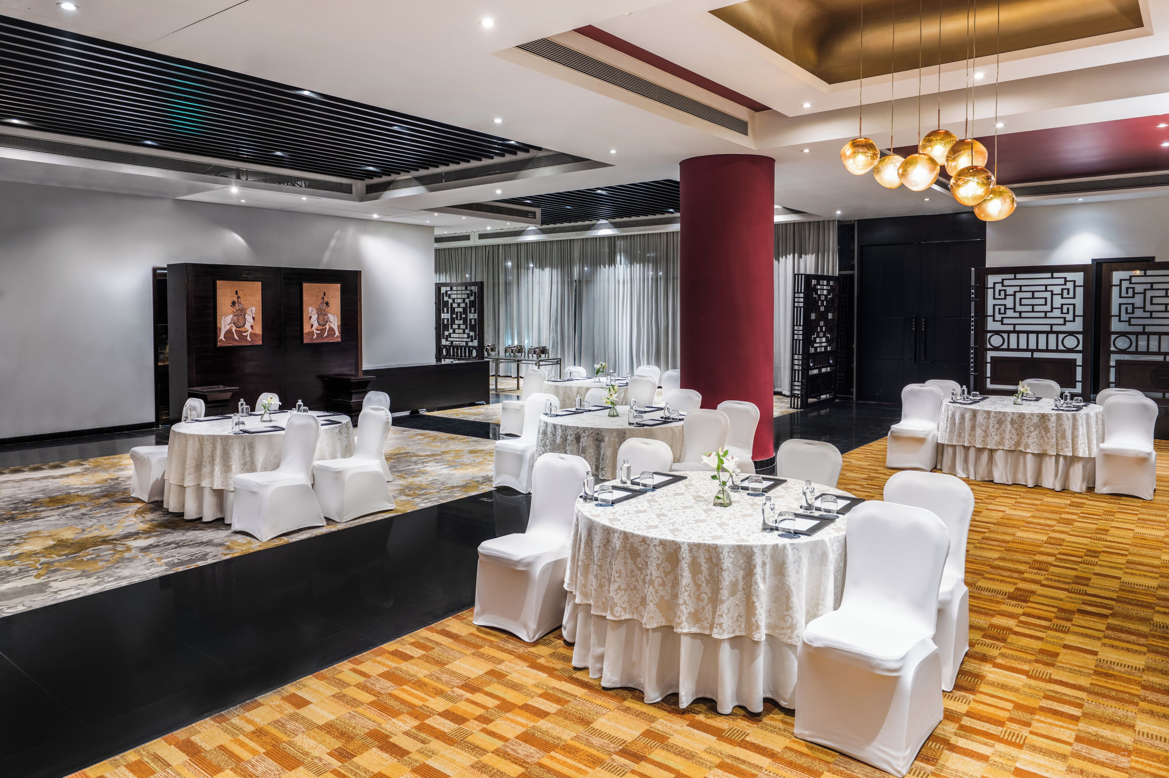 Un salón de banquetes con mesas redondas, sillas blancas y una alfombra estampada.