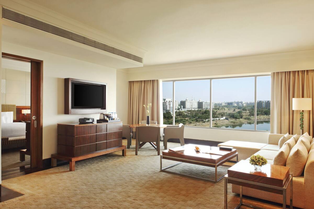 Habitación de hotel con un ventanal grande, un televisor de pantalla plana, un sofá, una mesa de centro y un mueble para televisión.