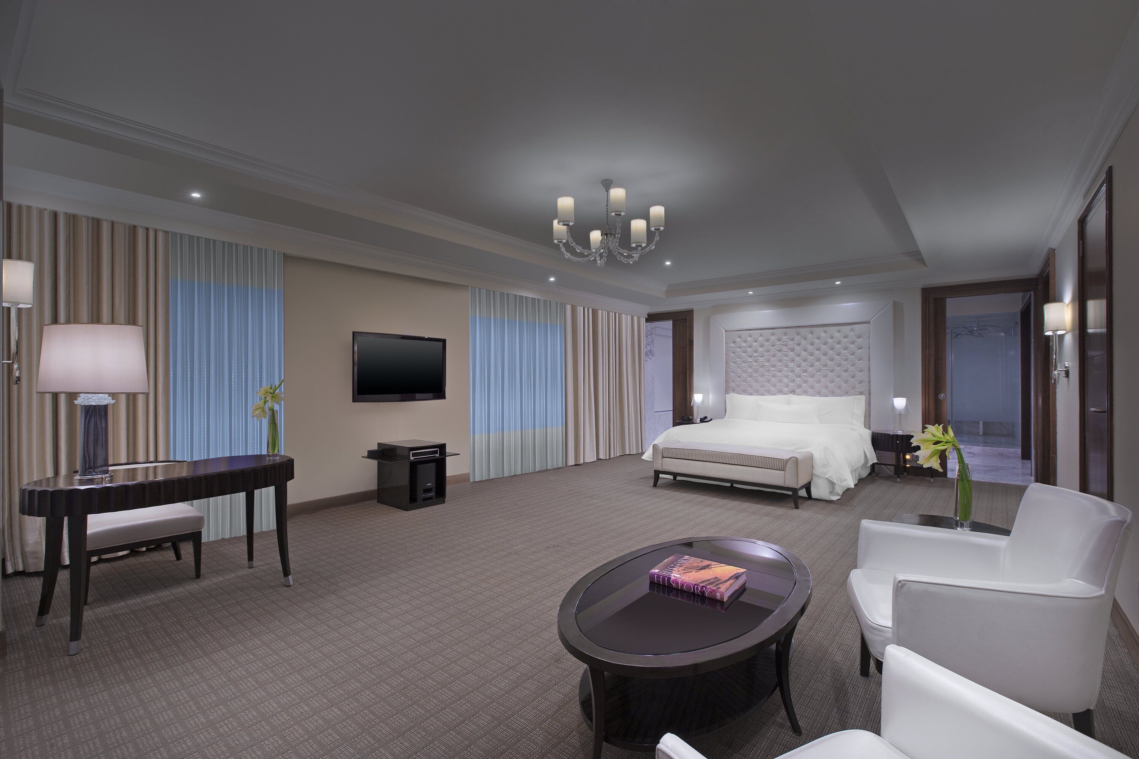 A hotel room with a bed, a desk, a chair, a coffee table, a TV, and a chandelier.