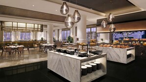 Un hall d’hôtel moderne avec un sol en marbre, un îlot central équipé d’ustensiles de cuisine et un espace détente avec des tables et des chaises.