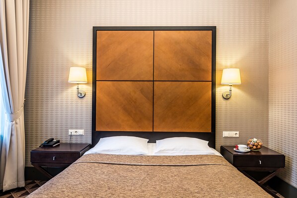 Una habitación de hotel con una cama grande, dos mesitas de noche, dos lámparas de pared y una mesita con teléfono y adorno decorativo.