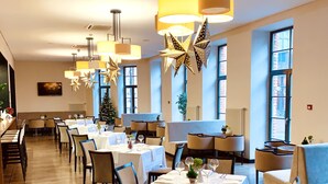 Un restaurante con varias mesas y sillas, un árbol de Navidad y ventanas amplias.
