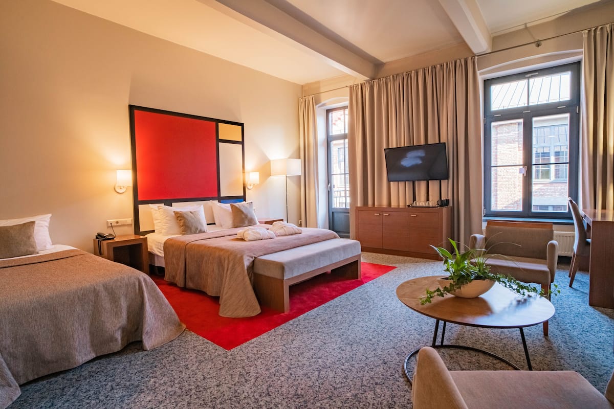 A hotel room with two beds, a TV, a desk, a chair, and a window with curtains.