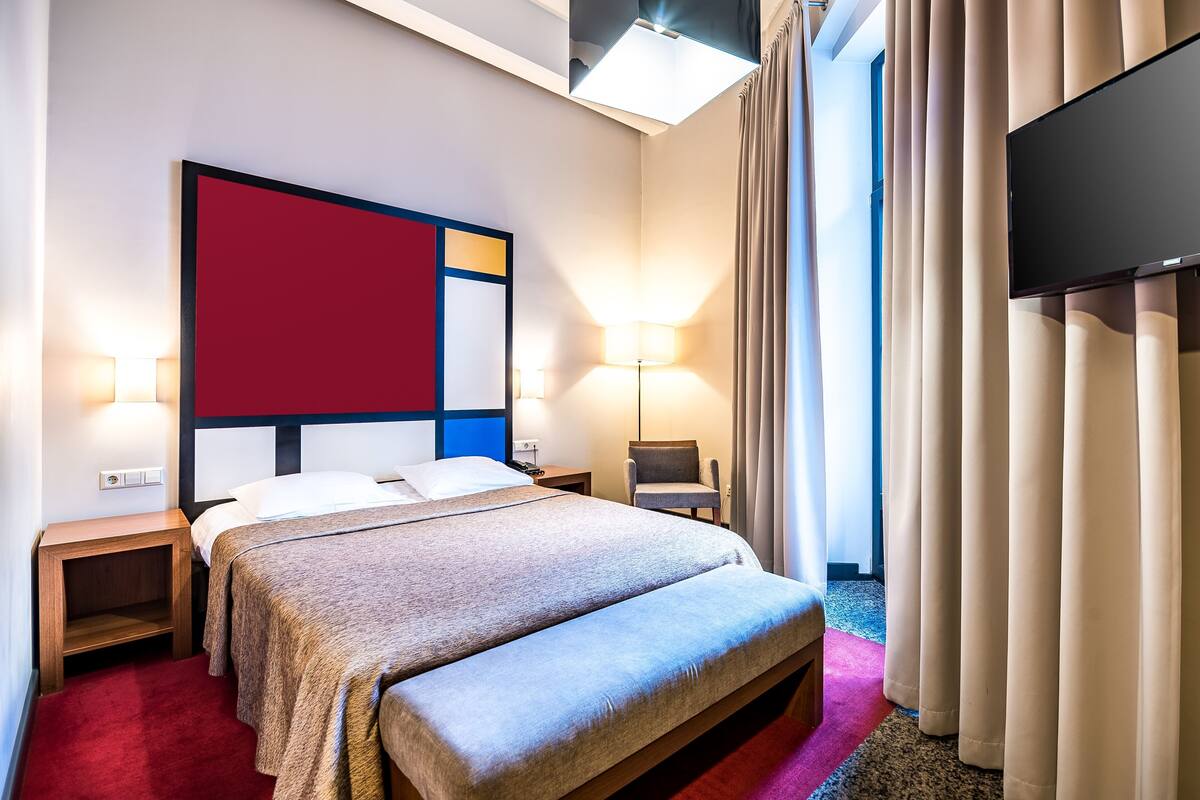 A hotel room with a bed, bedside tables, a TV, a lamp, and a chair.