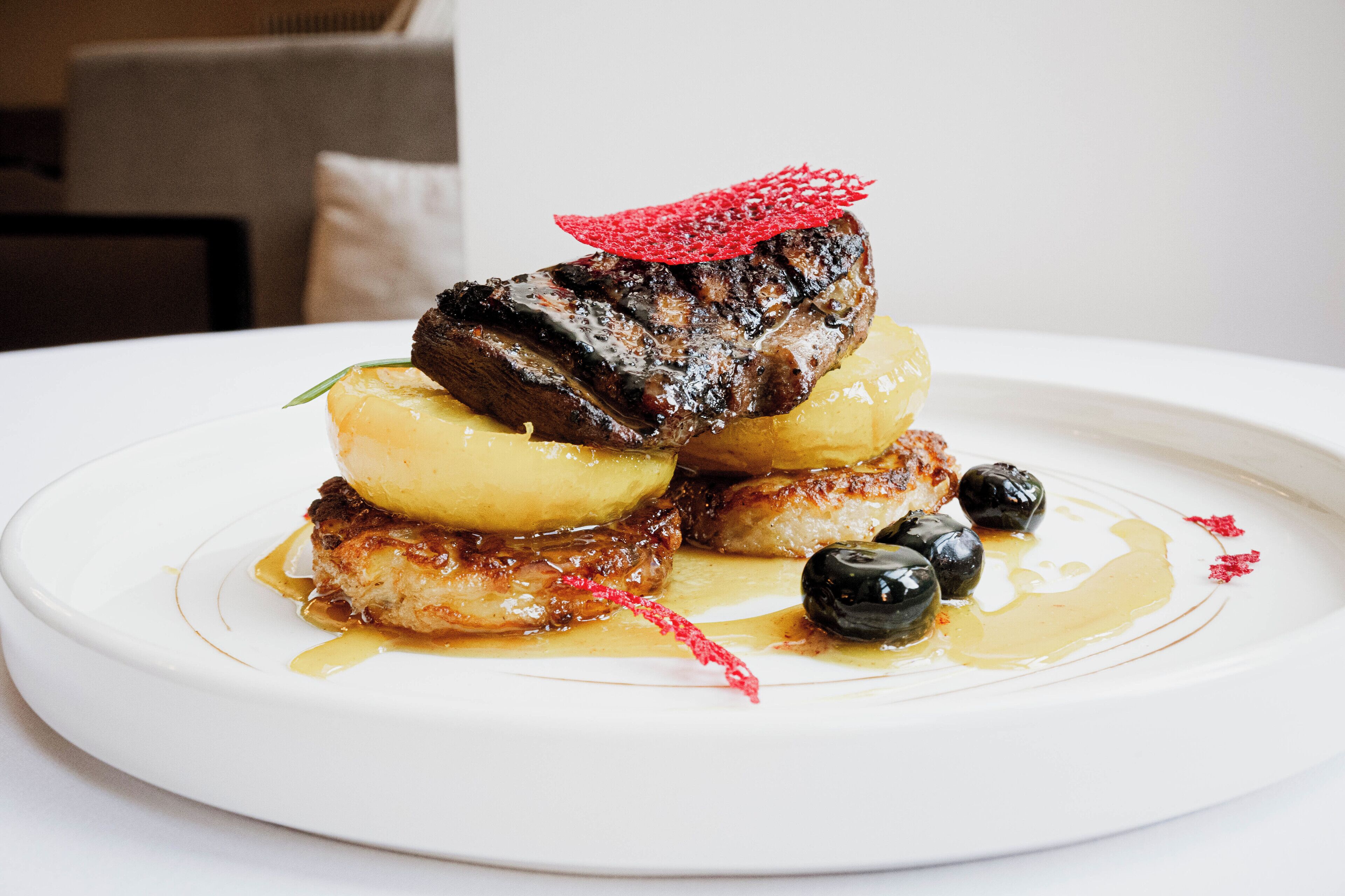 Un plato de comida con filete, patatas y aceitunas.
