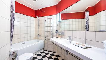 Un bagno moderno con pavimento a scacchi, pareti bianche e rosse, una vasca, una doccia e un mobile lavabo con asciugamani e articoli da toilette.