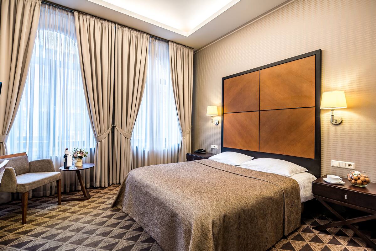 A hotel room with a large bed, a sofa, a small table with a lamp, and a nightstand with a lamp.