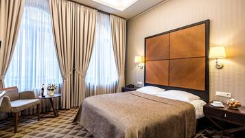 A hotel room with a large bed, a sofa, a small table with a lamp, and a nightstand with a lamp.