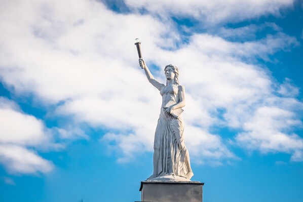 Una estatua de una mujer sosteniendo una antorcha, con cielo azul y nubes de fondo.