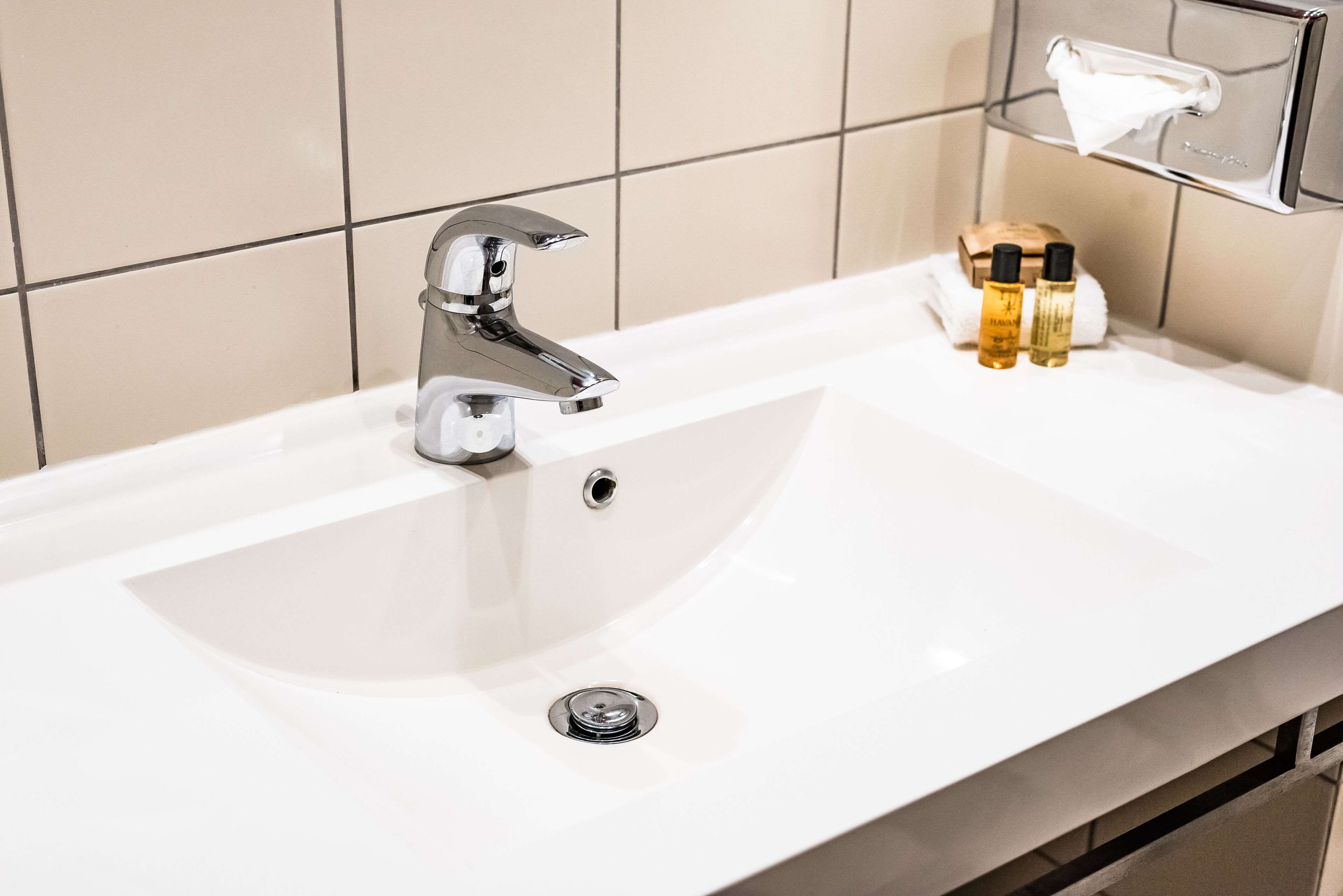 A bathroom sink with a chrome faucet, a mirror above it, and two bottles of liquid soap on the counter.