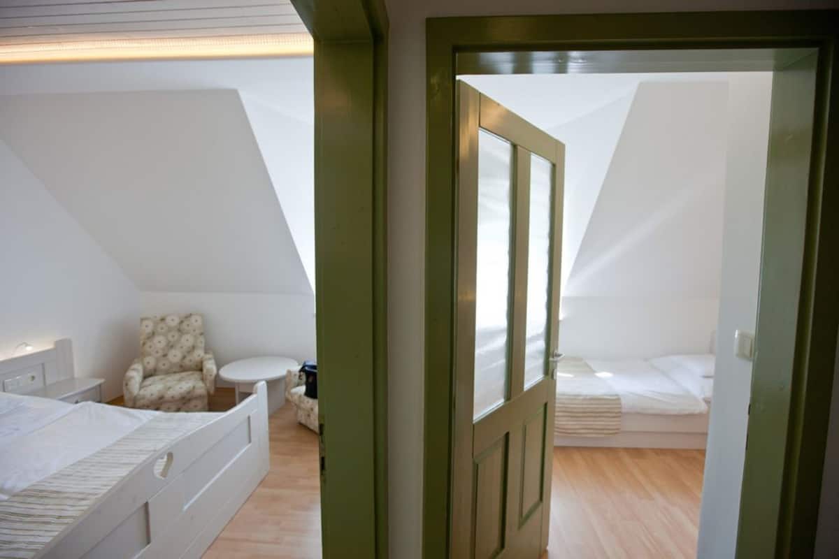 Un dormitorio con techo inclinado, una cama, una silla y una mesita.