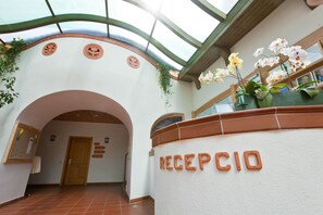 Uma área de recepção com uma placa com a inscrição 'RECEPCIO', uma porta de madeira e um chão ladrilhado.