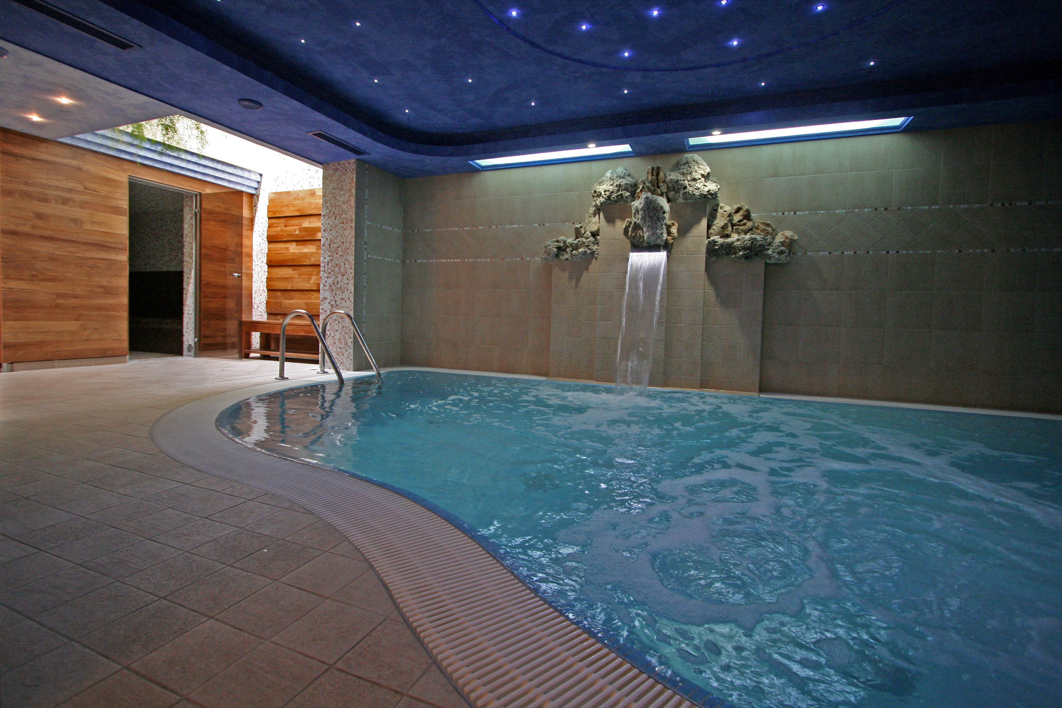 Ein Hallenbad mit Wasserfall, einer hölzernen Sitzbank und gefliestem Boden.