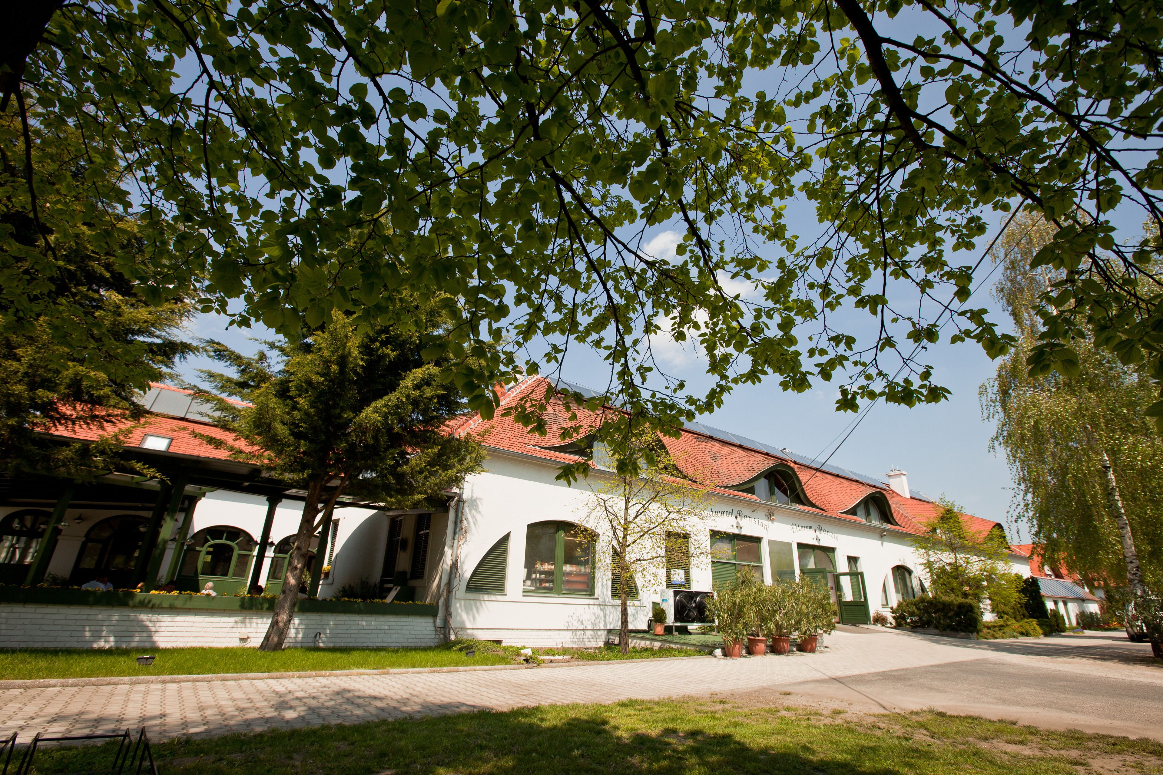 A white building with a red roof, green shutters, and a brick pathway leading to it.