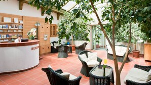 An indoor area with wicker furniture, a reception desk, and a potted tree. - Tornácos Panzió (HEGYKÖ)