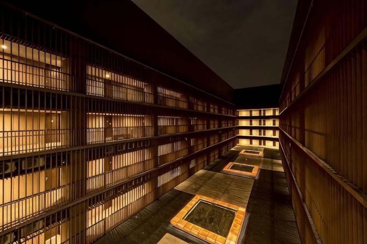Un pasillo con varias habitaciones, cada una con ventanas protegidas por barrotes y suelo de baldosas.