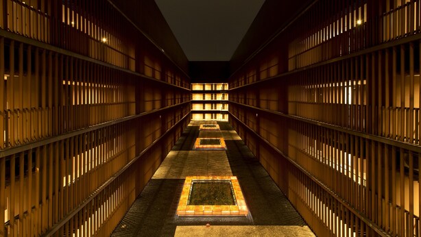 A long, narrow hallway with wooden paneling and illuminated windows on both sides, leading to a central open area.