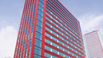 Ein modernes Hochhaus mit roter und blauer Fassade, das ein Raster aus Fenstern und einen auffälligen, vertikalen roten Streifen zeigt.