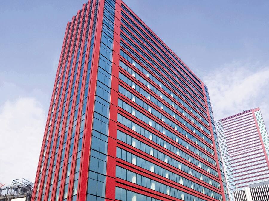 Ein modernes Hochhaus mit roter und blauer Fassade, das ein Raster aus Fenstern und einen auffälligen, vertikalen roten Streifen zeigt.