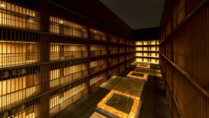 A corridor with multiple floors of rooms, each with barred windows and illuminated by warm lighting.