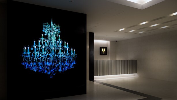 A modern lobby with a large illuminated blue chandelier, a reception desk, and a framed artwork on the wall.