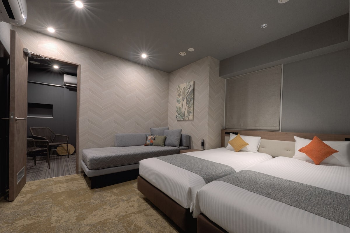 A modern hotel room with two beds, a seating area, and a large window.